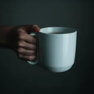 A person holding a white ceramic coffee mug by the handle wi