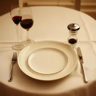 A dinner table scene with a plate, fork, knife, wine glass, 