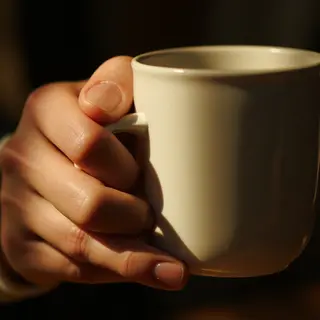A person holding a white ceramic coffee mug by the handle wi