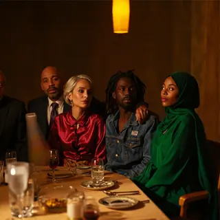 Four people at a dinner table: a bald man in a suit, a woman