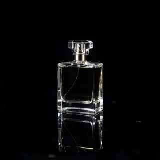 A clear glass perfume bottle on a reflective black surface w