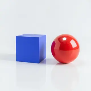 A red ball and a blue cube sitting side by side on a white s