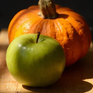 A green apple and an orange pumpkin on a wooden cutting boar