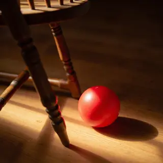 A red ball underneath a wooden chair