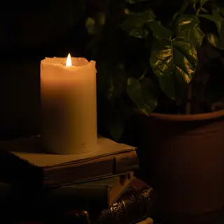 A candle on top of a stack of books, the books next to a pot