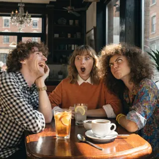 A group of three friends at a table: one laughing with head 
