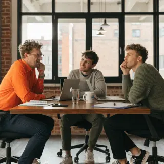 Three coworkers in a meeting: one looking frustrated with fu