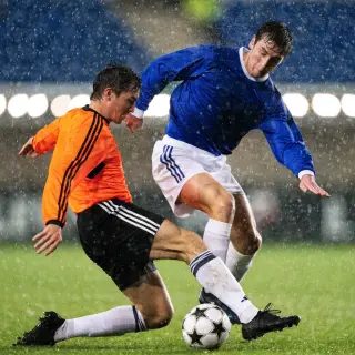 Two soccer players mid-tackle, one sliding and the other jum