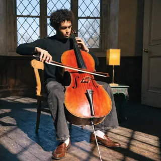 A cellist seated with correct posture, legs around the instr