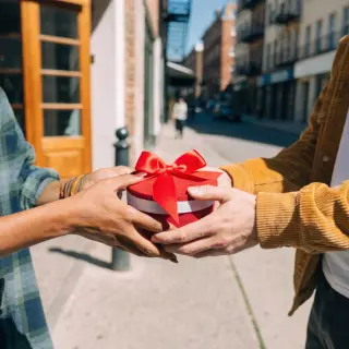 One person handing a small gift box to another person, both 