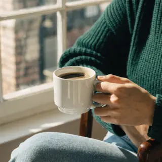 A person holding a white ceramic coffee mug by the handle wi