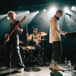 Three musicians on stage: a tall woman with short pink hair 