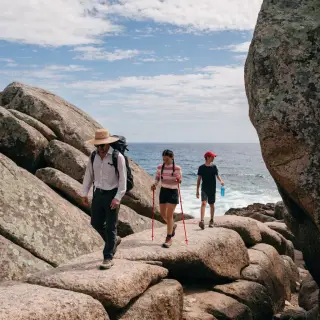 Three hikers on a trail: a man with a backpack and sunhat, a