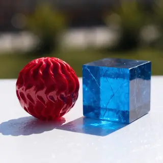 A red ball and a blue cube sitting side by side on a white s