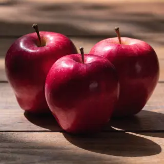 Exactly 3 red apples arranged on a wooden table