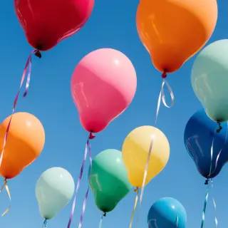 Exactly 11 colorful balloons floating against a clear blue s