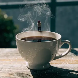 A tiny person standing on the rim of a coffee cup, looking d