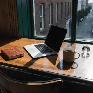 A workspace desk with a brushed aluminum laptop, a leather-b