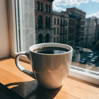 A coffee mug on a sunny windowsill casting a sharp shadow to