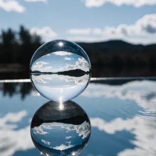 A clear glass sphere sitting on a mirror surface near a pool