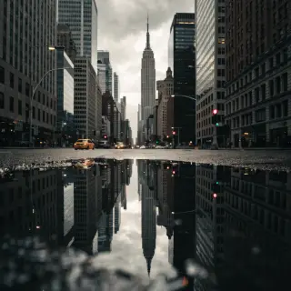 A city skyline reflected in a rain puddle on a street, with 
