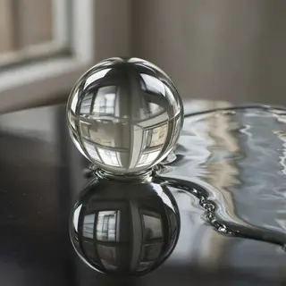 A clear glass sphere sitting on a mirror surface near a pool